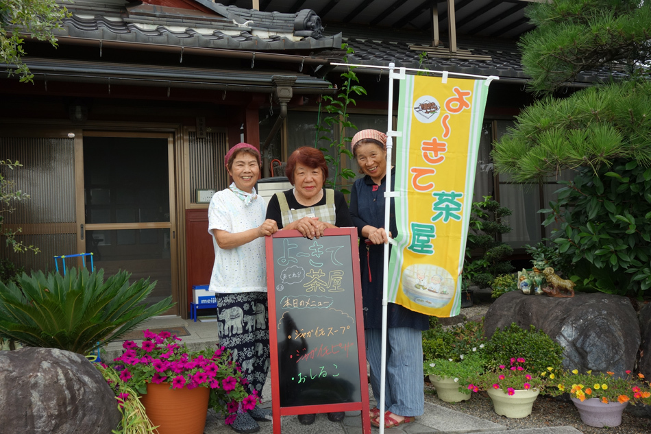 民家の前で幟と看板を持って立つ女性3人